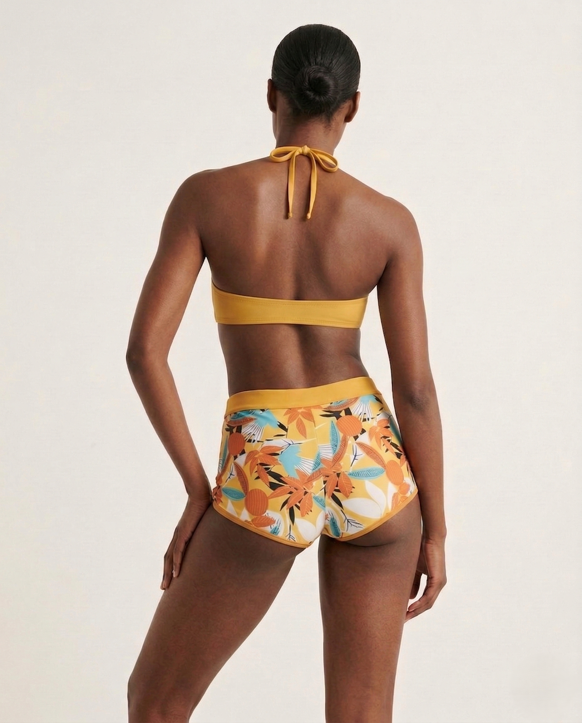 Model wearing a flirty halter bikini with soft botanical print and bow detail on a sunny beach